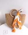 Close-up of semi-circular straw bag with woven handles and geometric silk scarf detail - Coffee + Carriage Orange Scarf