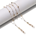 Golden eyewear chain with white pearls and geometric beads on a white pedestal - Polygon Design