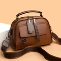 Borsa a mano in pelle marrone con tracolla a righe e ciondolo a canguro su sfondo beige - Cuoio