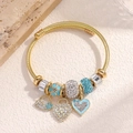 Detalle de pulsera de cable dorada con colgantes de candado de corazón y flores azules - Estilo de Esmalte de Corazón Azul (80521802)