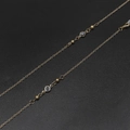 Detail of golden eyeglass chain with clear crystal beads and lobster clasp on black surface - White