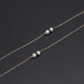 Goldene Brillenkette mit weißen Perlen und schwarzen Ringelementen auf schwarzem Grund - Gold Perle Schwarz Kreis Stil