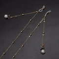 Golden metal glasses chain with white pearls and crown charms on black background - Gold