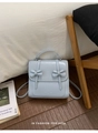 Detail of light blue backpack featuring symmetrical bows and elegant flap closure - Blue