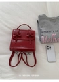 Detail of red glossy leather backpack with bow accents and top handle on white fabric - Red