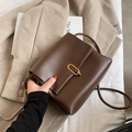 Chic dark brown leather crossbody bag with golden oval clasp on beige background - Coffee