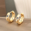 Goldene Huggie-Ohrringe mit Stern-Gravuren und blauen Zirkonia auf einer Texturoberfläche - Gold