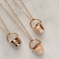 Macro shot of rose gold bucket pendants with FUCKIT BUCKET engraving on marble - Bucket + Necklace / Rose Gold