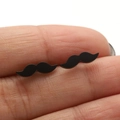 Macro shot of black mustache stud earrings on a fingertip showing tiny size and sleek finish - Mustache Style (679) / Black