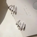 Dettaglio di orecchini a lobo in argento a quattro griffe con linee curve e micro zirconi - Oro Bianco