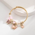Detailaufnahme eines goldenen Armreifs mit rosa Kristall-Schmetterling und Herzanhängern - Rosa