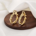 Klassische goldene gedrehte Creolen mit Federverschluss auf einem Holzständer - Gold