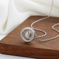 Collier à pendentif sphère rotative argentée sur fond de bois et tissu blanc plissé - Or Blanc