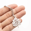 Close-up of polished stainless steel monstera leaf keychain in hand over white background - Steel