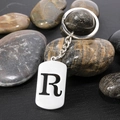 Stainless steel keychain with hollow letter R pendant over natural pebbles - Letter R