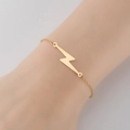 Primer plano de pulsera minimalista de acero inoxidable dorado con colgante de rayo en la muñeca - Dorado