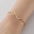 Primer plano detallado de una pulsera minimalista de acero inoxidable dorado con onda - Dorado