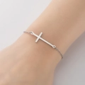 Primer plano de una pulsera minimalista de plata con cruz en la muñeca de una mujer joven - Color Acero