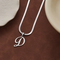 Collana a catena piatta d'argento con ciondolo lettera D corsiva su sfondo marrone - Lettera D