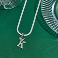 Silver crown letter K pendant with flat snake chain necklace on a green background - Letter K