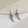 Pendientes largos de acero inoxidable con alas de ángel huecas sobre soporte blanco - Color Acero