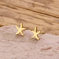 Macro shot of polished gold starfish stud earrings resting on a natural stone surface - Gold