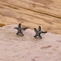 Macro shot of minimalist starfish stud earrings in dark metal on a textured surface - Black