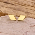 Vista macro de pendientes geométricos dorados minimalistas sobre piedra natural - Dorado
