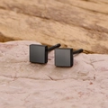 Vista macro de pendientes de botón cuadrados negro mate minimalistas sobre piedra - Negro