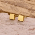 Primer plano de pendientes de tuerca cuadrados dorados minimalistas sobre piedra - Dorado