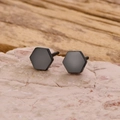 Vista macro di orecchini a lobo esagonali neri opachi minimalisti su pietra naturale - Nero