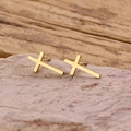 Detail of minimalist gold cross stud earrings resting on a natural pink stone surface - Gold