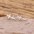 Polished stainless steel cross stud earrings for men and women on a rustic stone background - Steel