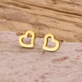 Dettaglio degli orecchini a cuore dorati traforati su pietra con sfondo in legno naturale - Oro
