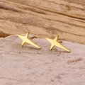 Minimalist gold four-pointed star stud earrings displayed on a textured pink stone - Gold