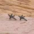 Detail shot of minimalist black matte star stud earrings on a natural stone base - Black