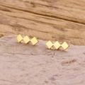 Detail van gouden geometrische ruitvormige oorbellen op steen en hout achtergrond - Goud