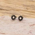 Detailed close-up of minimalist black gear stud earrings on a textured stone surface - Black