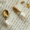 Vue macro des boucles d'oreilles perles dorées avec gravure S925 sur page de livre ancien - Or 18K / Doré