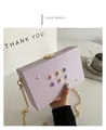 Elegante bolso caja morado con flores 3D y cadena dorada, mostrado sujeto con la mano - Morado