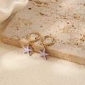 Gros plan de boucles d'oreilles étoile de mer dorées avec émail lavande sur une surface en pierre - Boucles d'Oreilles Créoles Étoile de Mer Mauves (Paire)