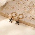 Gros plan de boucles d'oreilles étoiles de mer dorées avec émail noir sur pierre - Boucles d'Oreilles Créoles Étoile de Mer Noires (Paire)
