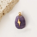 Violetter Amethyst-Tropfenanhänger mit goldenem Blitzsymbol auf beigem Steinhintergrund - Amethyst Blitz