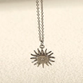 Macro shot of silver sun pendant featuring a peaceful face and classic cross chain - Sun Face / Steel