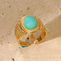 Macro view of a gold-tone stainless steel ring featuring a turquoise stone and carved details - Blue