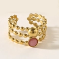 Detail eines mehrlagigen Gold-Titanstahlrings mit rosa Opalperle und polierter Metallkugel - Gold mit rosa Edelstein