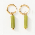 Primer plano de aros dorados con elegantes colgantes cilíndricos de piedra natural verde - verde claro
