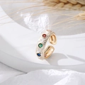 Macro shot of gold adjustable ring with white enamel, heart patterns and colorful gems - White
