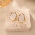 Detail view of oval gold earrings with white marble inlay on a stone pedestal - Irregular Stud Earrings Pair - White