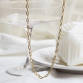 Elegante gouden paperclip schakelketting gepresenteerd met minimalistische luxe decoratie - Paperclip Ketting / Goud